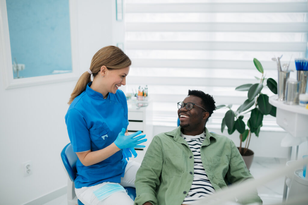 A female dentist giving some good news to her male patient about the state of his dental health, while he's listening to her with a toothy smile on his face