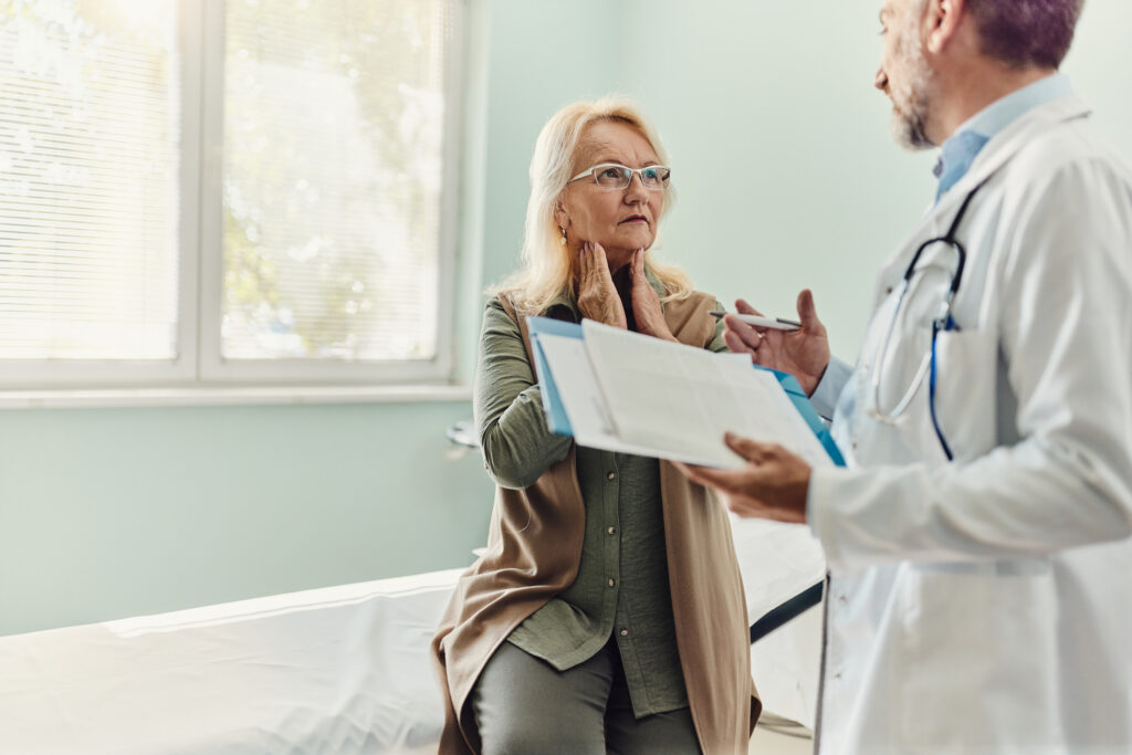 Senior woman with sore throat talking to her doctor during an appointment in hospital.